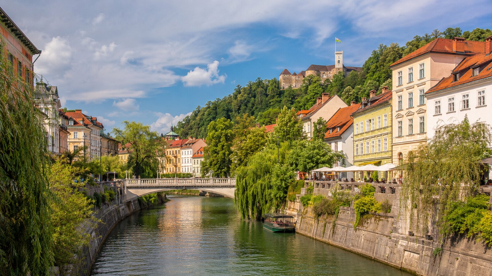 Řeka Ljubljanica s mosty a nábřežím v Lublani, v pozadí hrad
